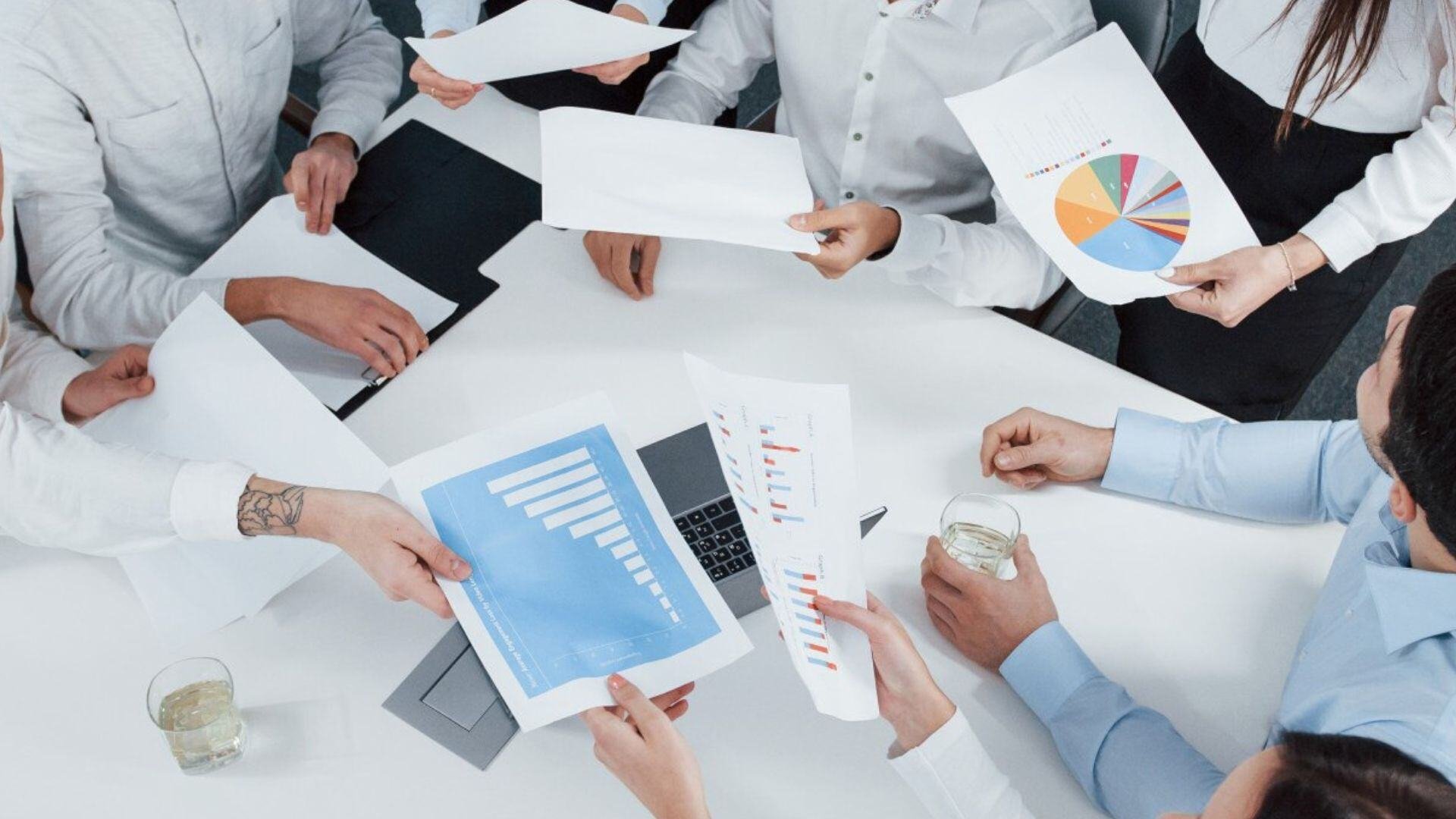 Reunión de equipo en oficina, compartiendo gráficos y documentos financieros para planificación estratégica.