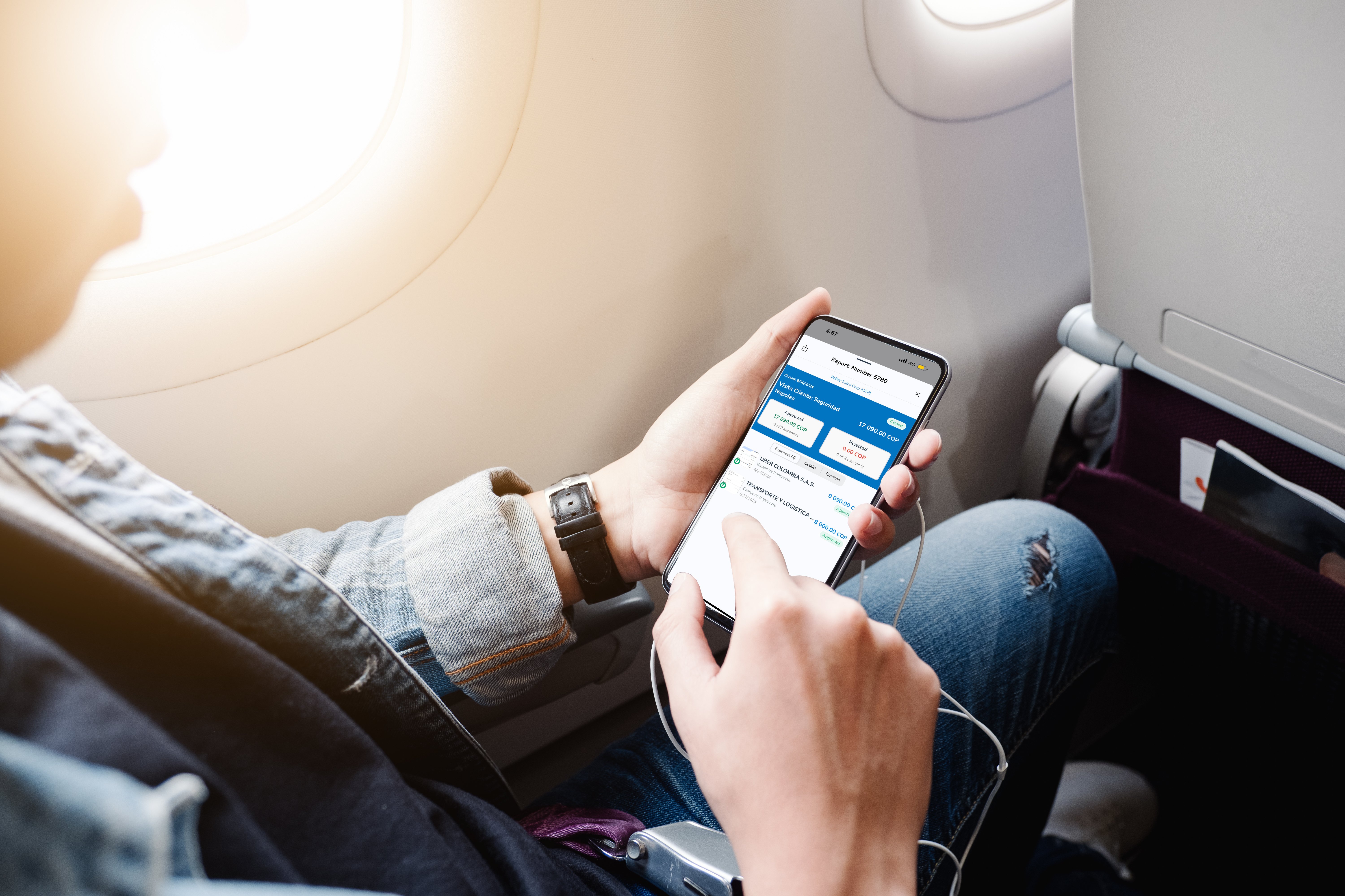 Persona usando un teléfono móvil en un avión, con la pantalla mostrando una interfaz de gestión de viáticos en Rindegastos.