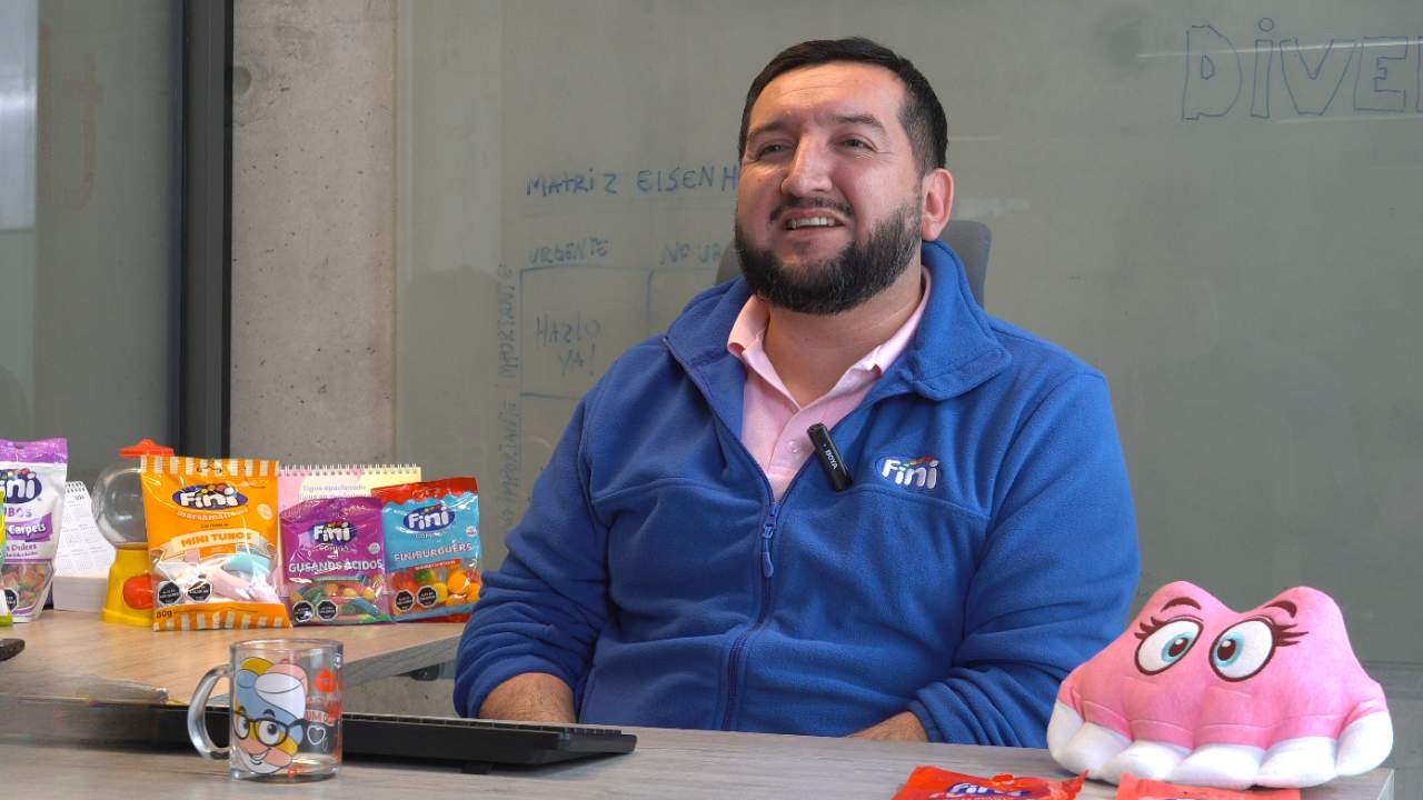  Ejecutivo de Fini con uniforme corporativo azul en su oficina, rodeado de productos y merchandising de la marca, en una entrevista sobre innovación, logística y operación comercial.