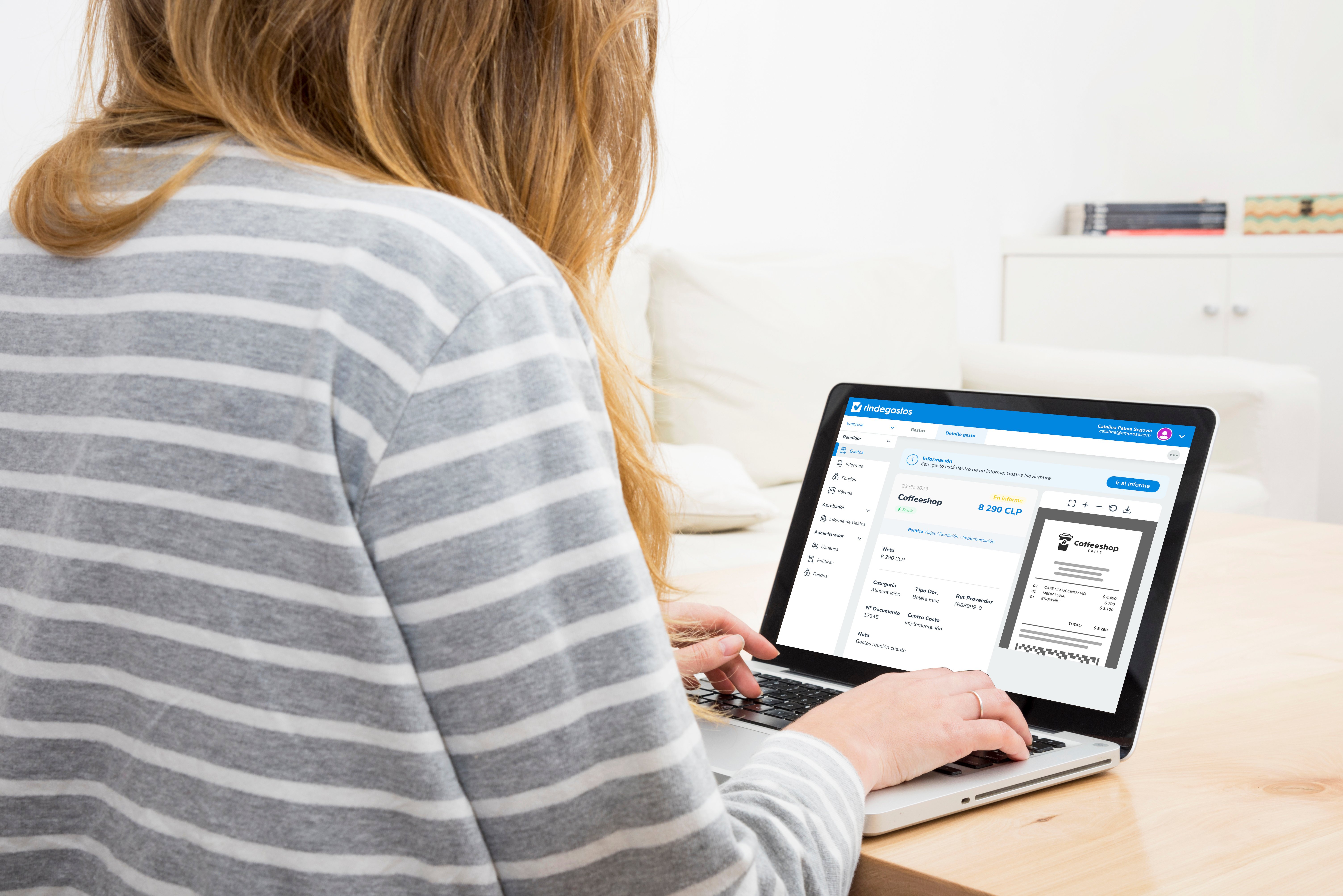Mujer de cabello largo y suéter de rayas usando una laptop con la interfaz de Rindegastos, mostrando un detalle de viáticos registrados y un recibo escaneado.