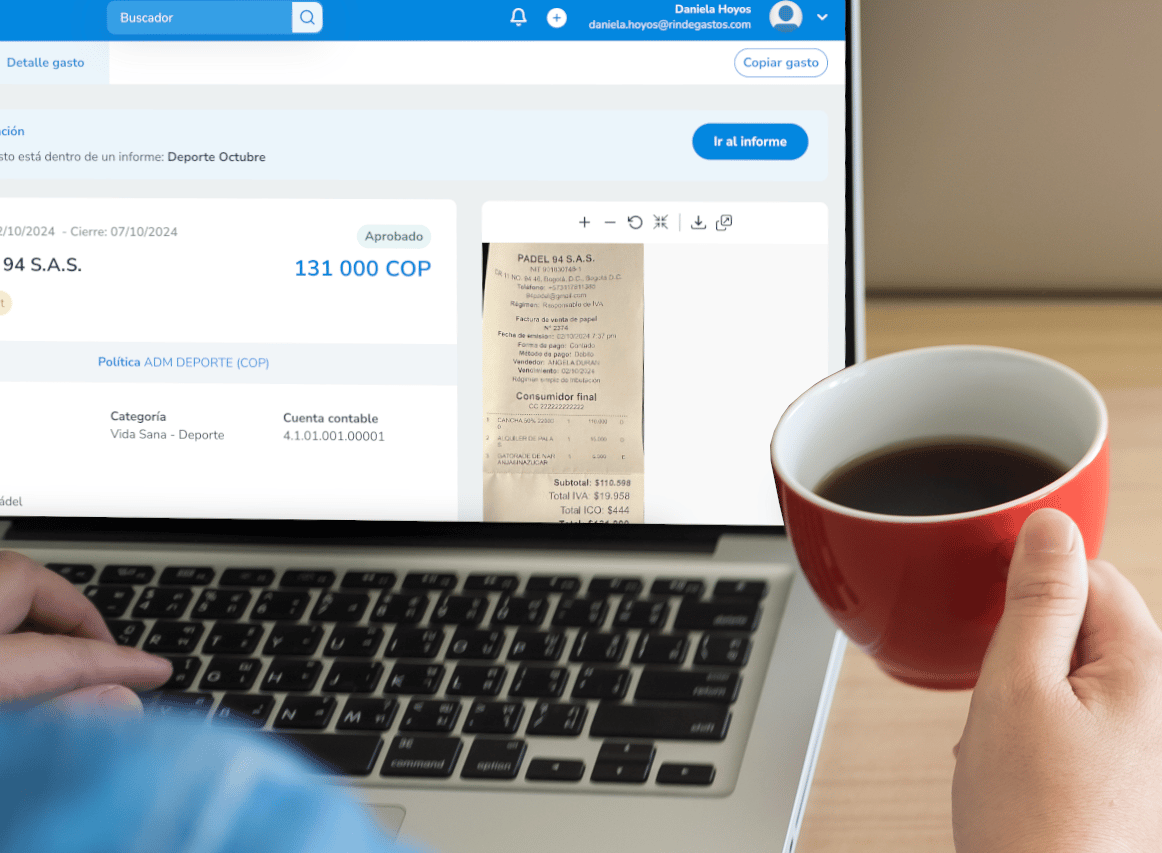 Persona usando una laptop mientras sostiene una taza de café, visualizando una rendición de gastos aprobada en la plataforma Rindegastos, con una factura escaneada visible en pantalla.