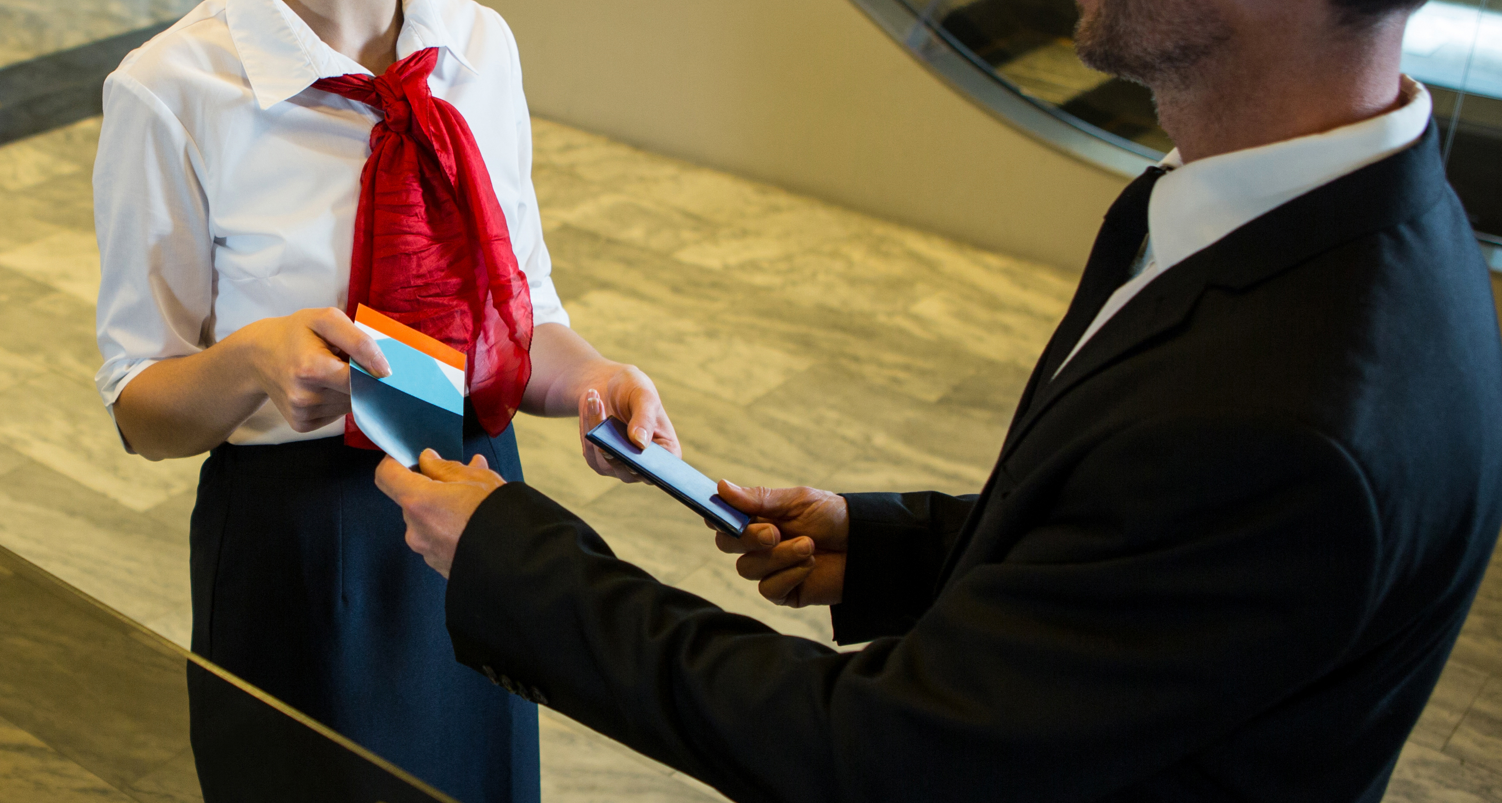 Agente de aeropuerto sonriente entregando el pase de abordar y pasaporte a un hombre de negocios en el área de check-in.
