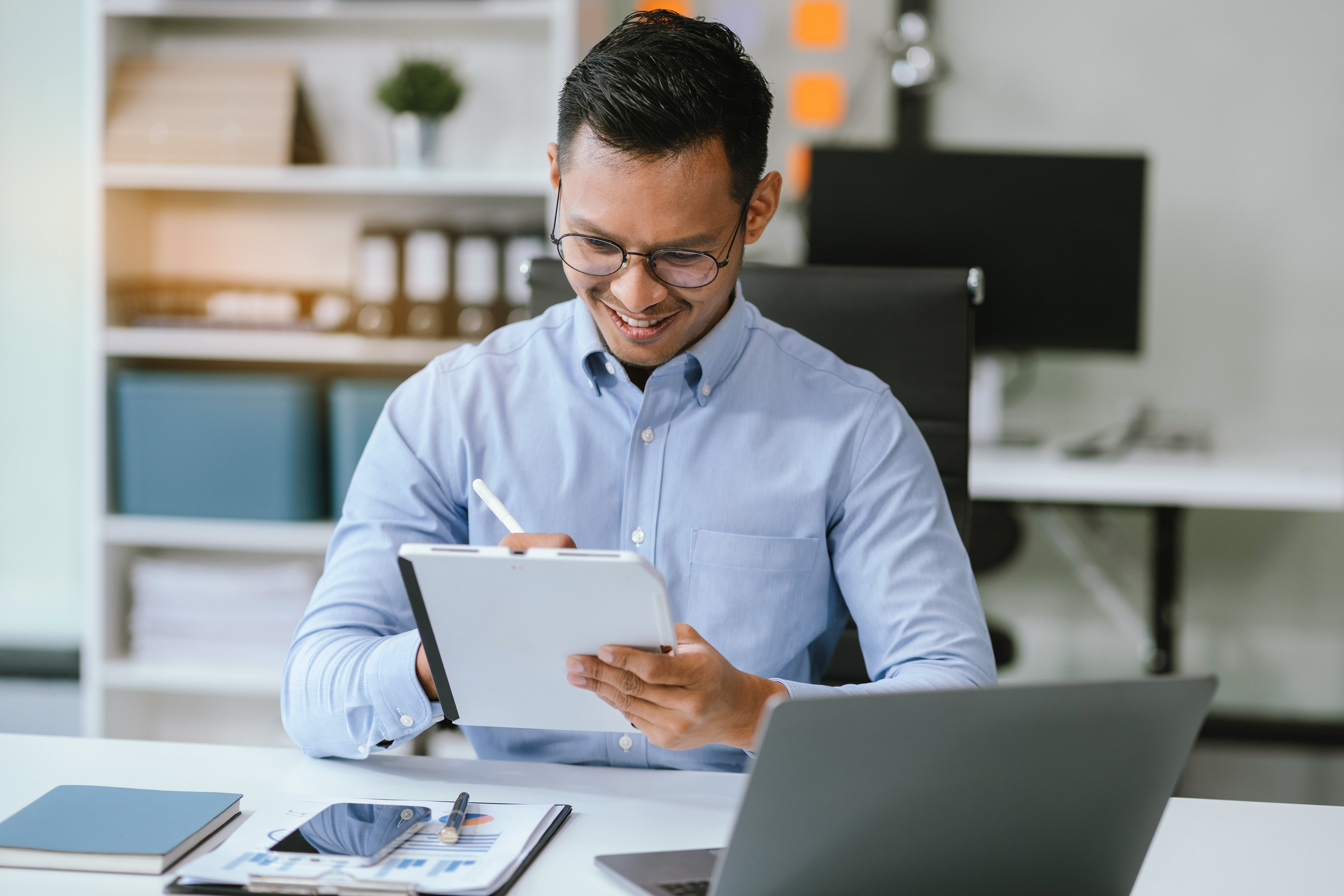 Dos personas trabajando en una oficina abierta, una usando una calculadora mientras la otra trabaja en su laptop, con documentos y gráficos financieros sobre la mesa.