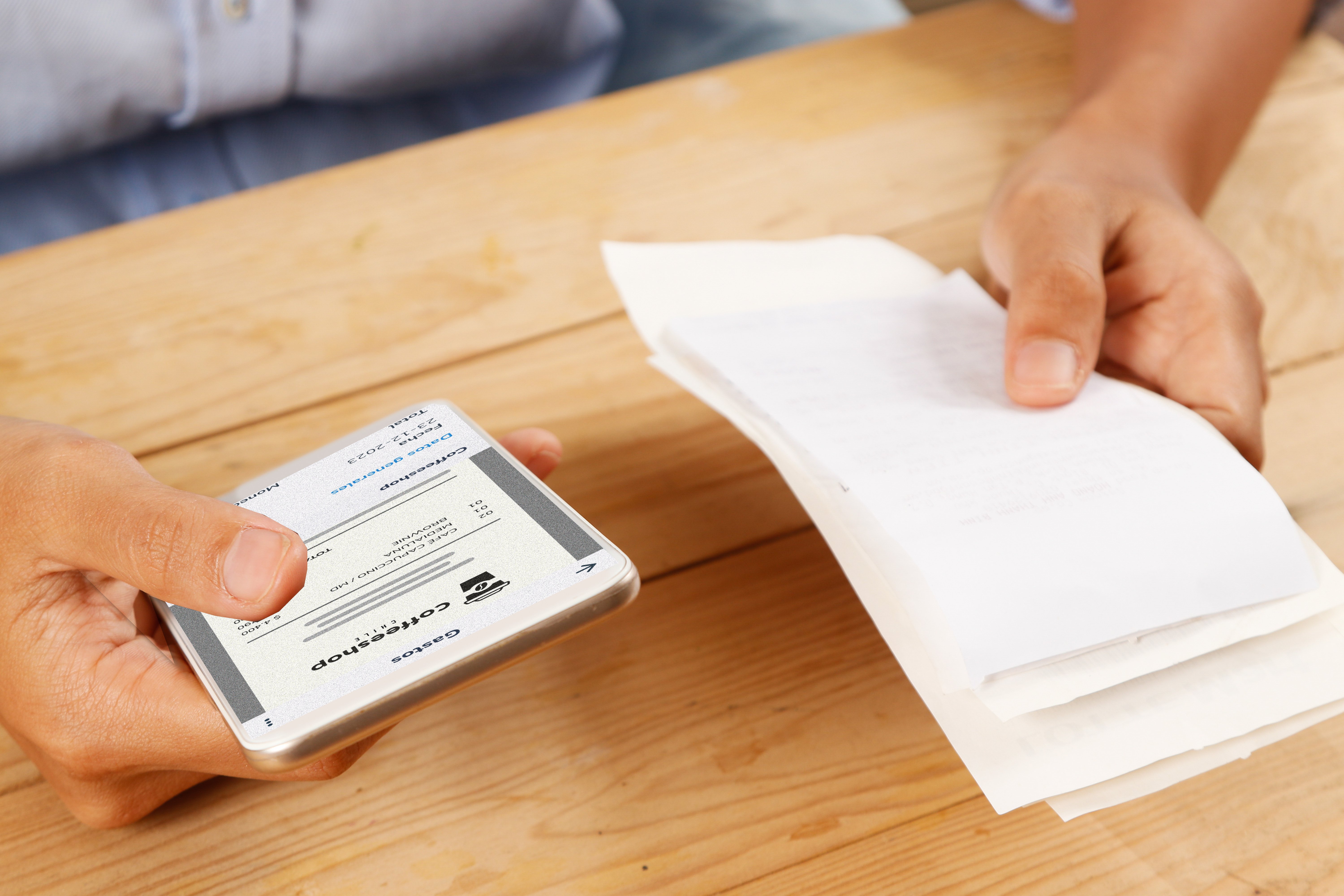 : Persona digitalizando un recibo con su celular mientras sostiene varios comprobantes en papel, representando la gestión digital de gastos.