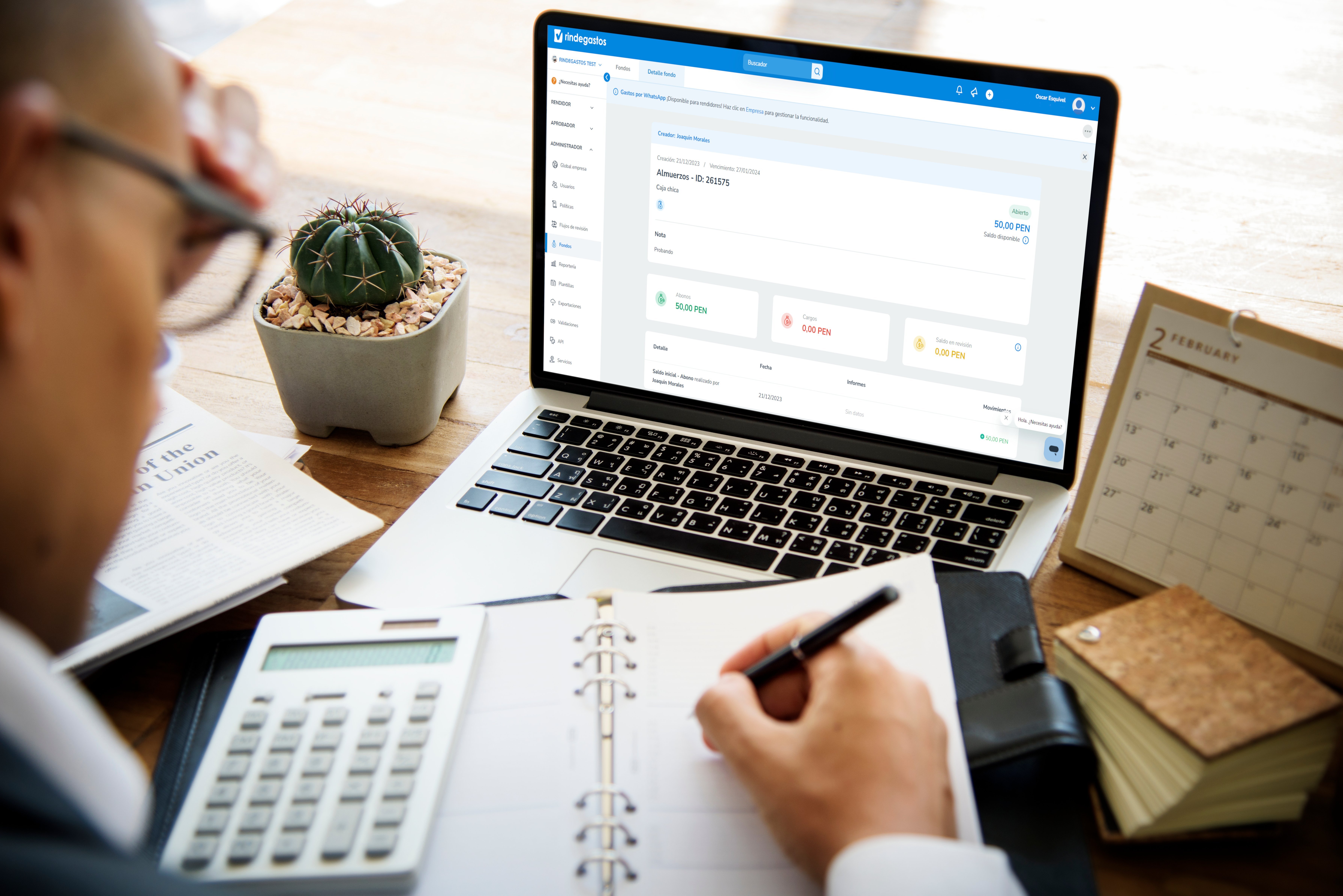 Persona escribiendo en una agenda frente a una laptop con la plataforma Rindegastos abierta, junto a una calculadora, cactus y calendario de escritorio.