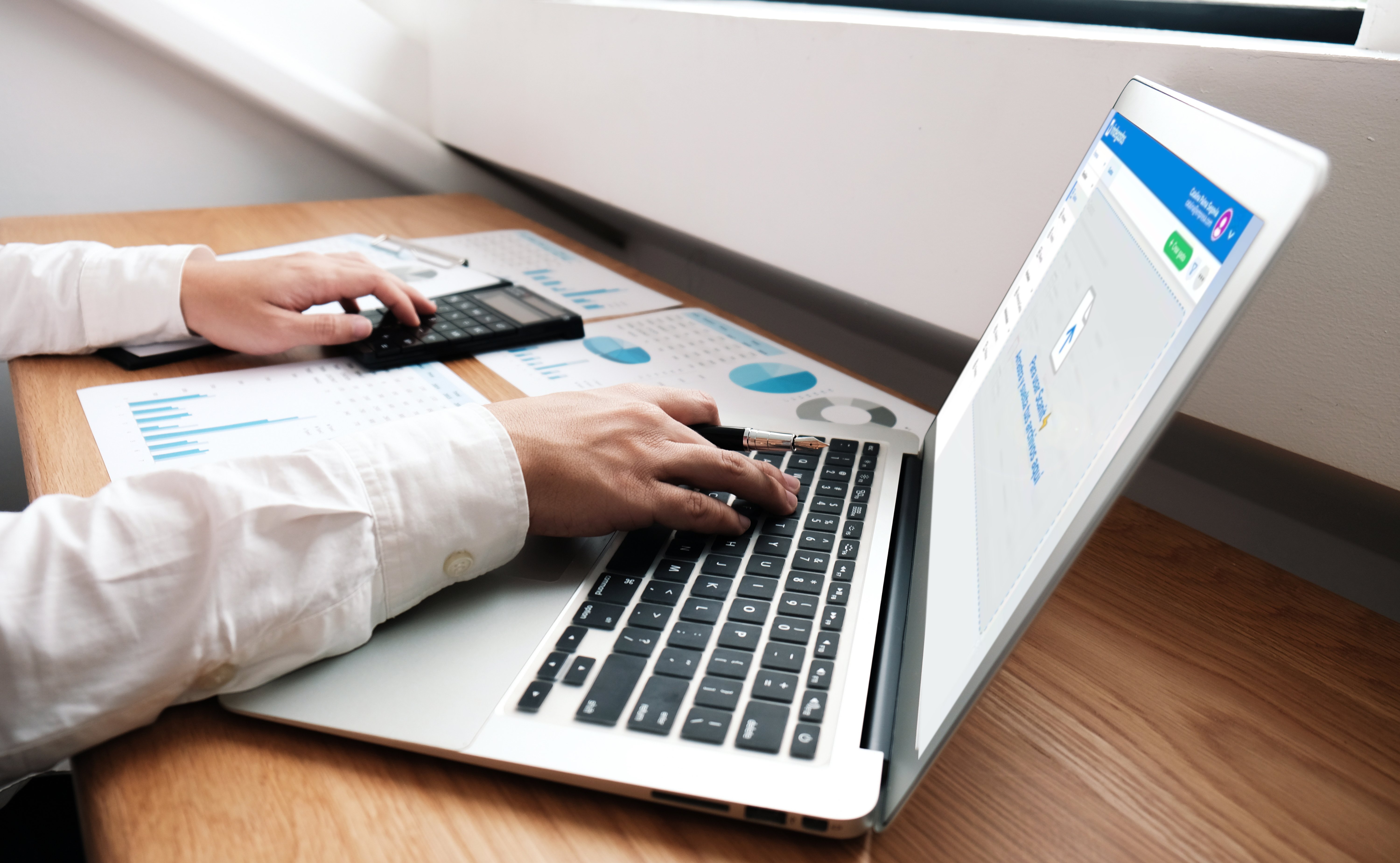 Persona trabajando en una laptop revisando gráficos financieros mientras usa una calculadora, con la plataforma de Rindegastos abierta en pantalla