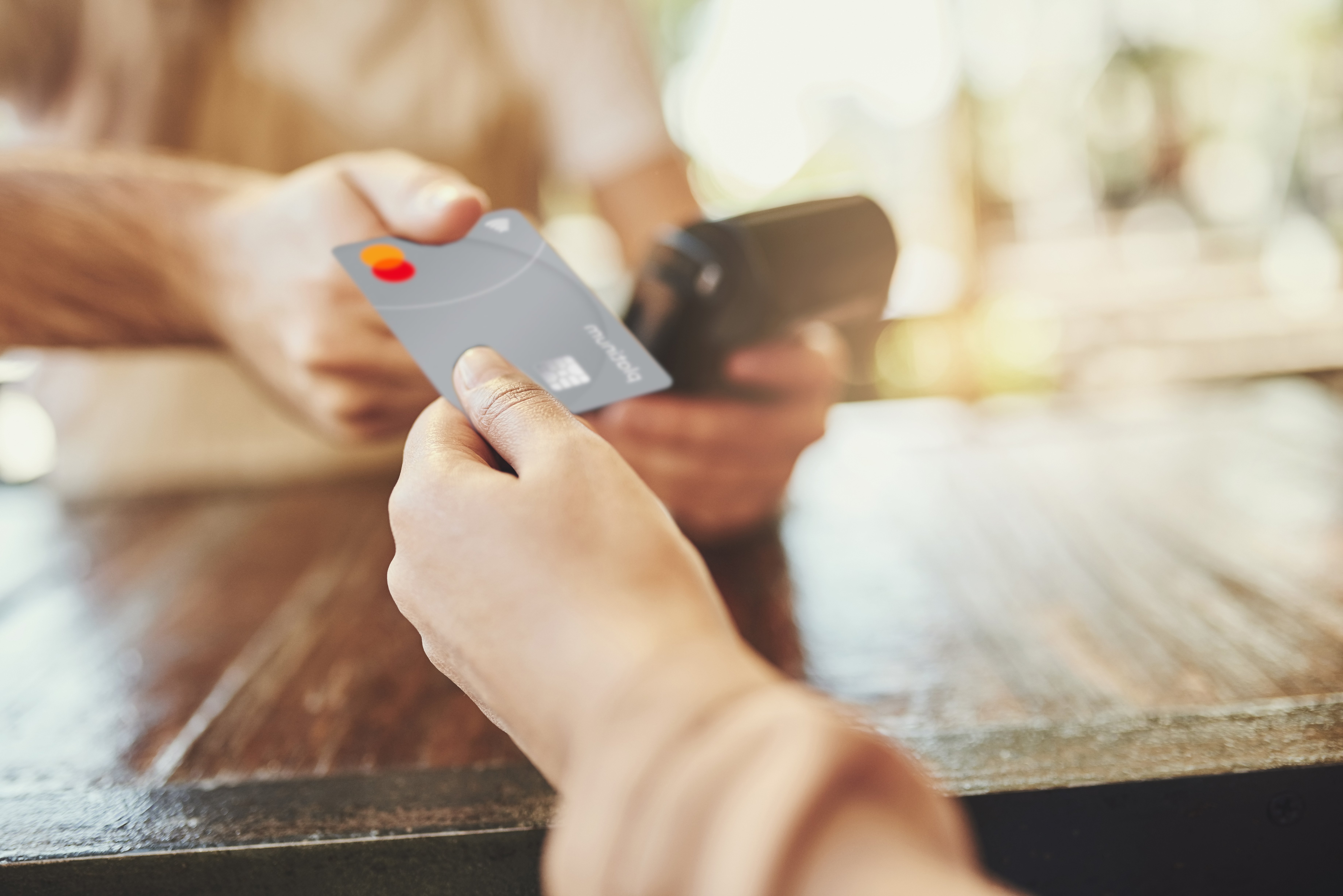 "Mano sosteniendo una tarjeta Mastercard acercándola a un dispositivo de pago, representando una transacción corporativa