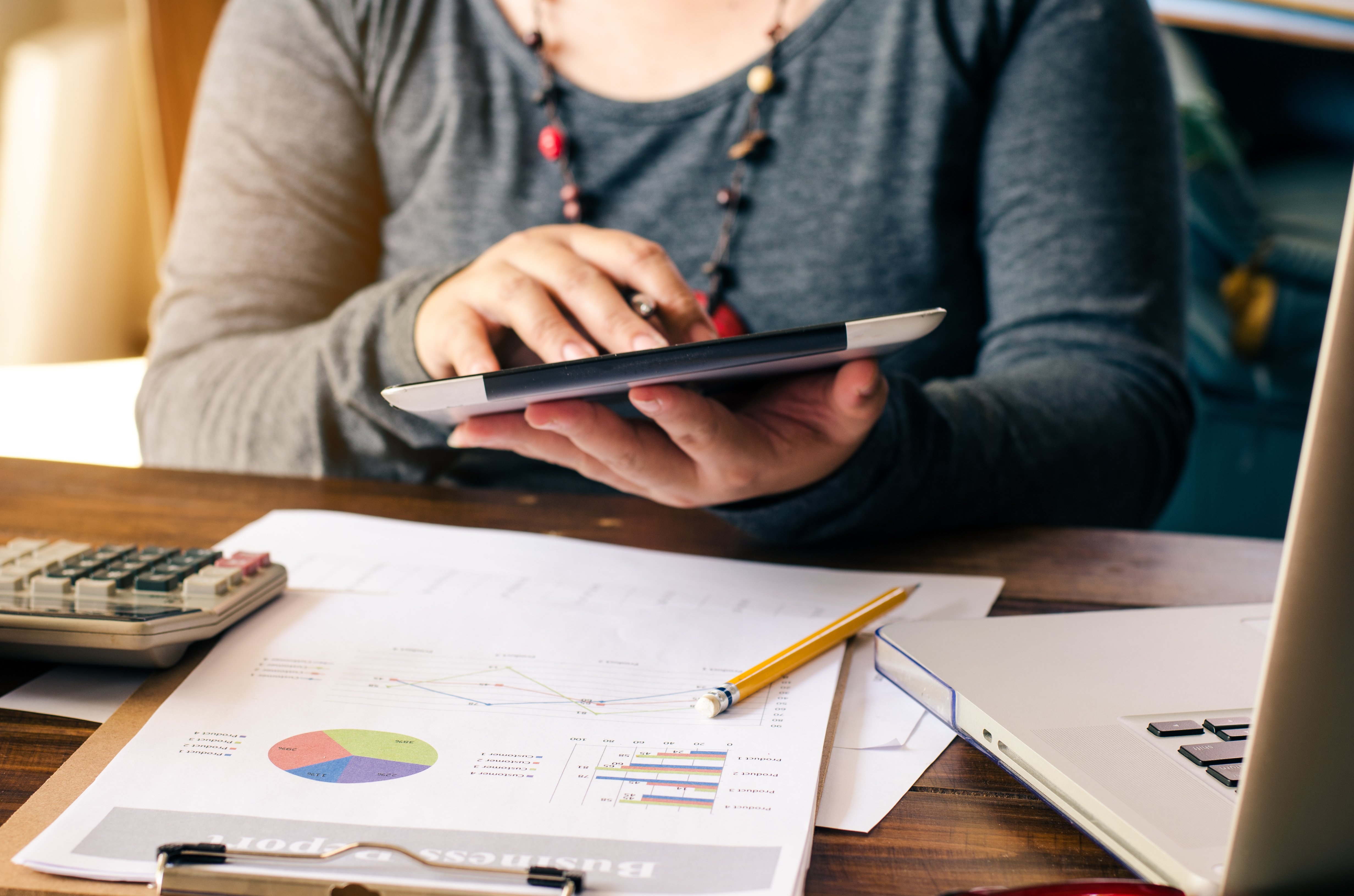 Persona usando una calculadora en una tableta mientras revisa gráficos financieros impresos, posiblemente trabajando en la gestión de presupuestos o gastos.